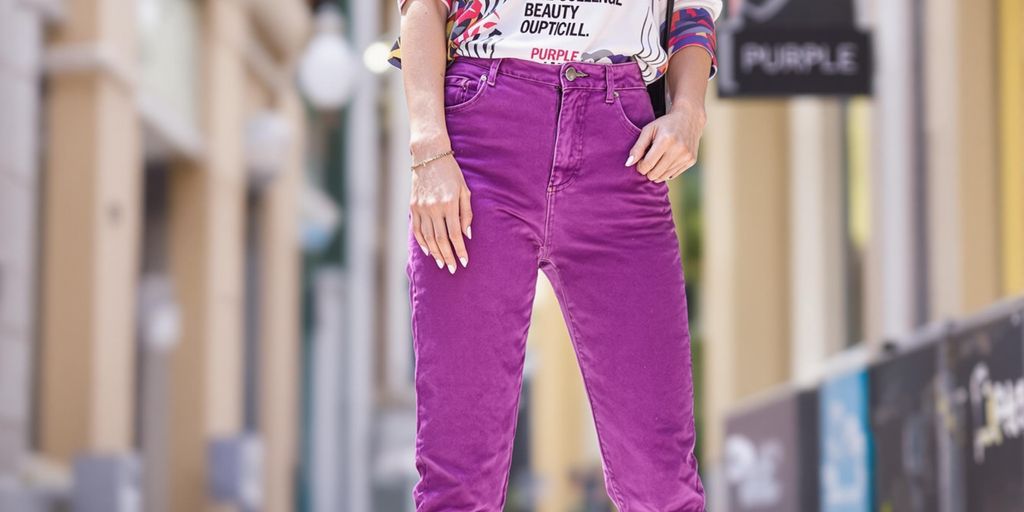 Model in purple jeans against a colorful urban setting.